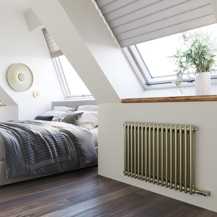 Anthracite designer radiator installed below a roof window in a loft bedroom with a bed, dark flooring and a potted plant.