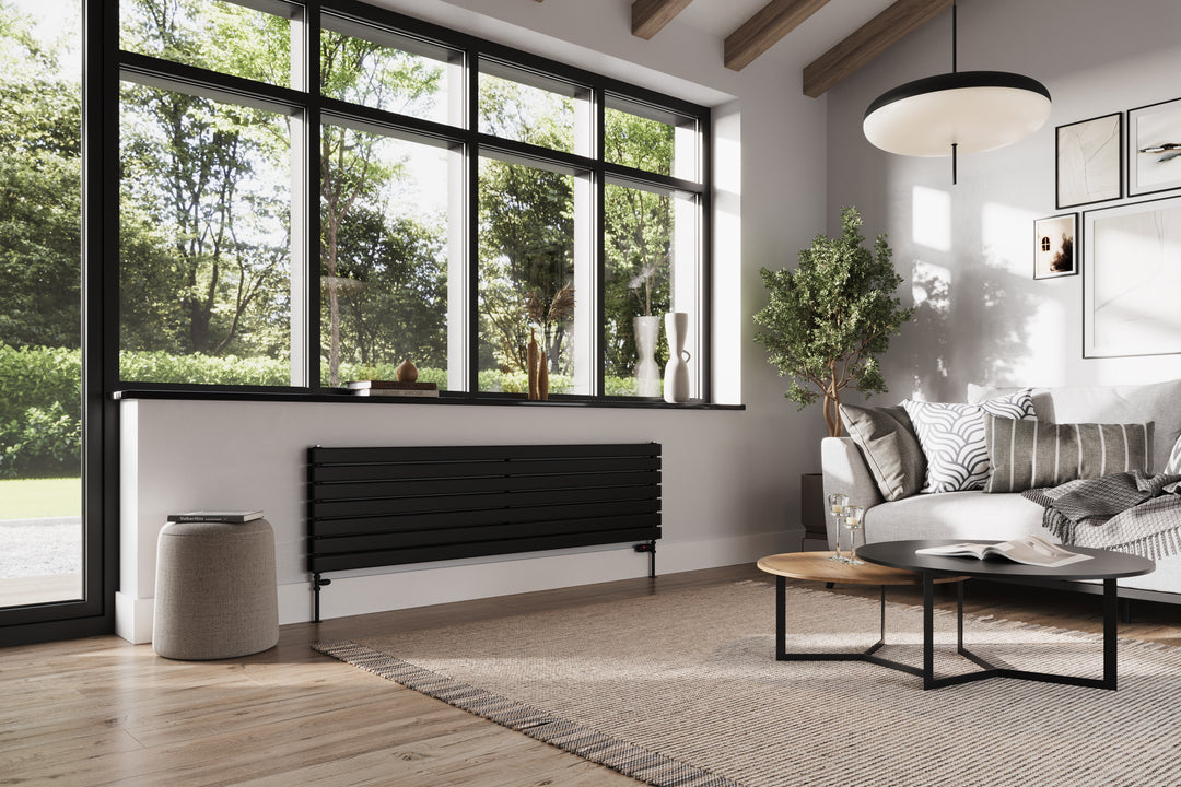 A black horizontal radiator in a room with a neutral palette, full of natural light, wooden beams, Scandi features, and green plants.