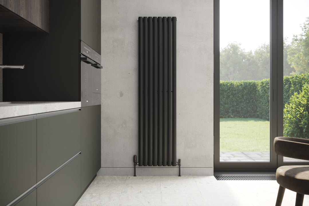 A black vertical radiator against a grey wall in an industrial-style kitchen with dark cabinets and tile floors.