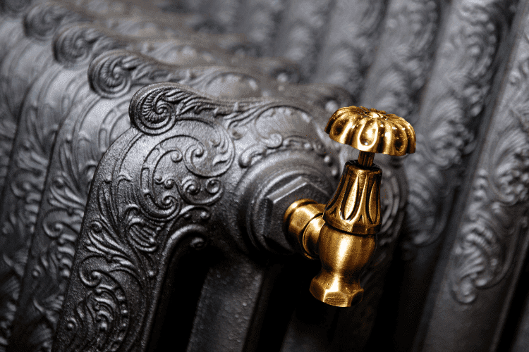  Close-up of a decorative cast iron radiator with intricate scrollwork and a polished brass valve.