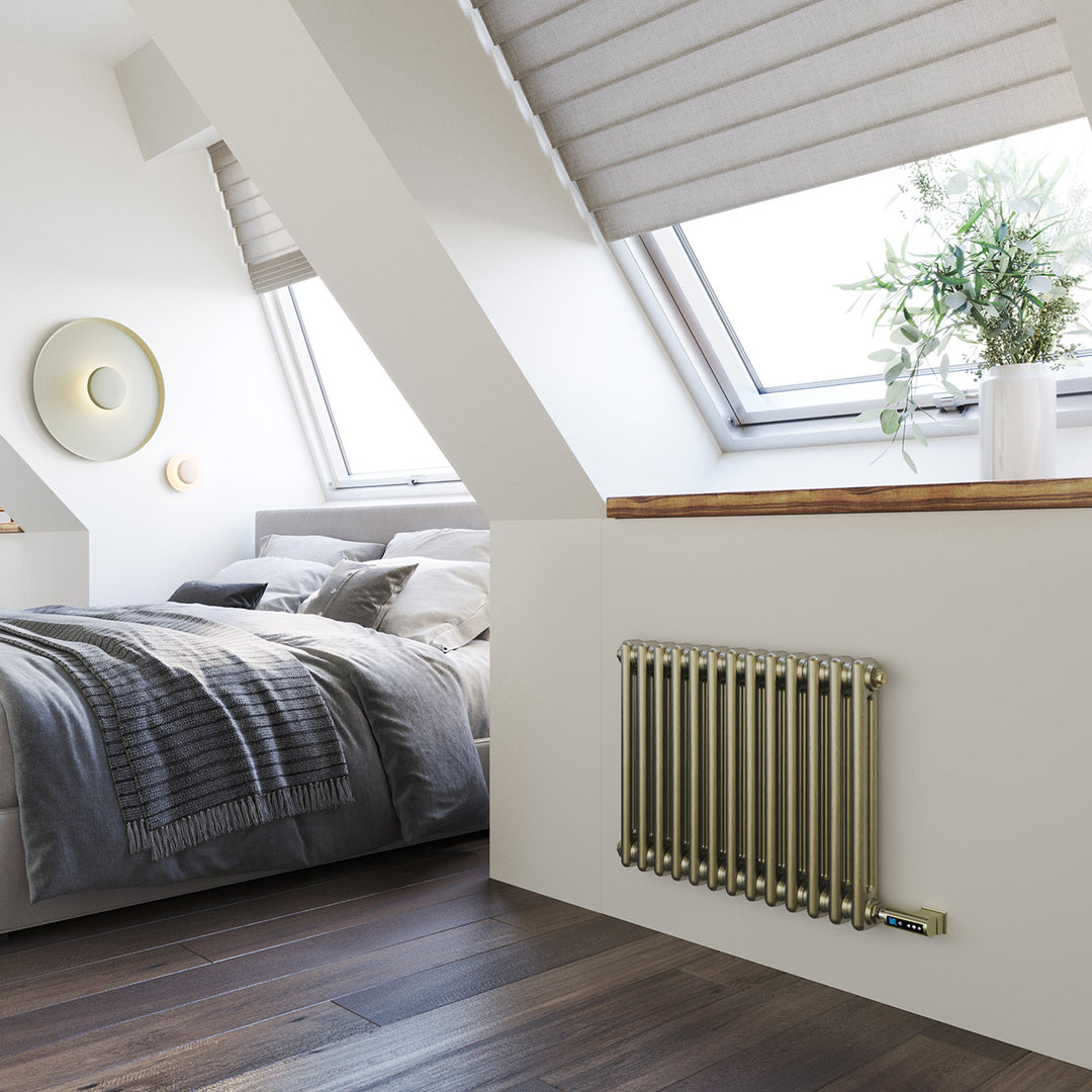 Anthracite designer radiator installed below a roof window in a loft bedroom with a bed, dark flooring and a potted plant.